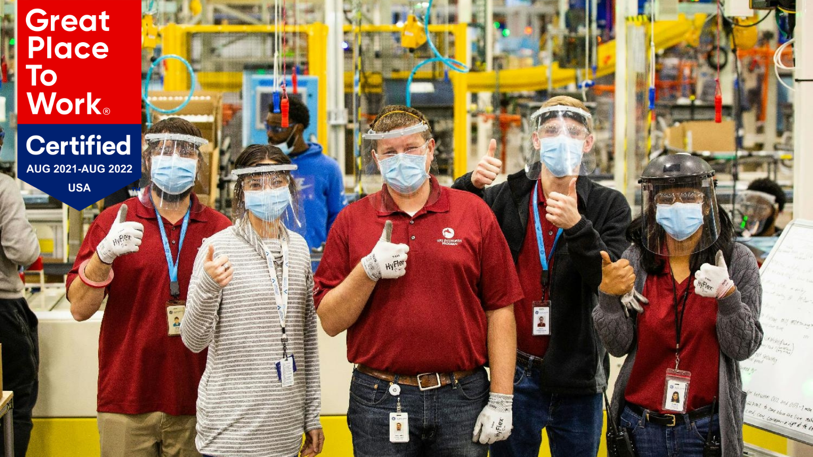 Employees wearing PPE in plant gather with thumbs up