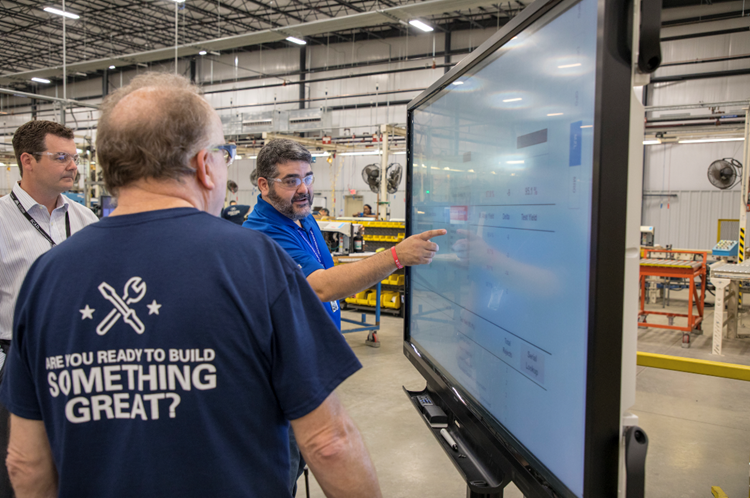 Real-Time Visibility for Smarter Factory Decisions Three men look at a digital monitor in the manufacturing facility for Real-Time Visibility for Smarter Factory Decisions